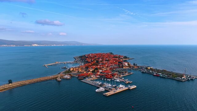Historic island city with red roofs and marina facilities. Aerial shot of an old town situated on an island connected by a bridge featuring a marina and boats.