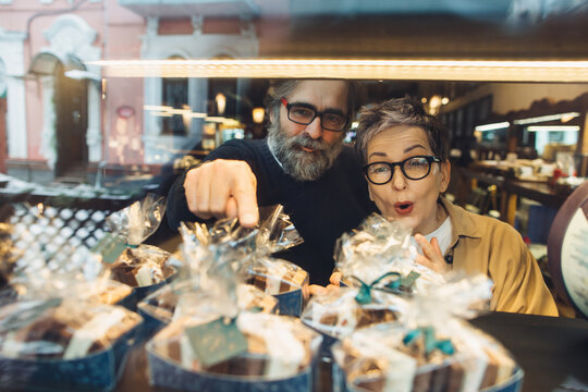 Mature couple choosing sweet treats in bakery window