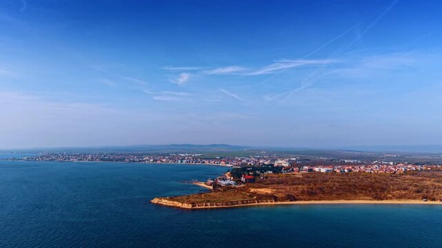 Wide aerial panorama of a coastline and sandy beach. Panoramic view of a long sandy coastline with a small peninsula extending into the blue sea under a clear sky.