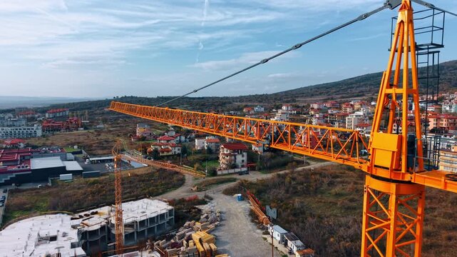 Yellow tower crane jib over coastal town landscape. Close-up of a yellow tower crane jib and trolley system with a residential town and hills in the background.