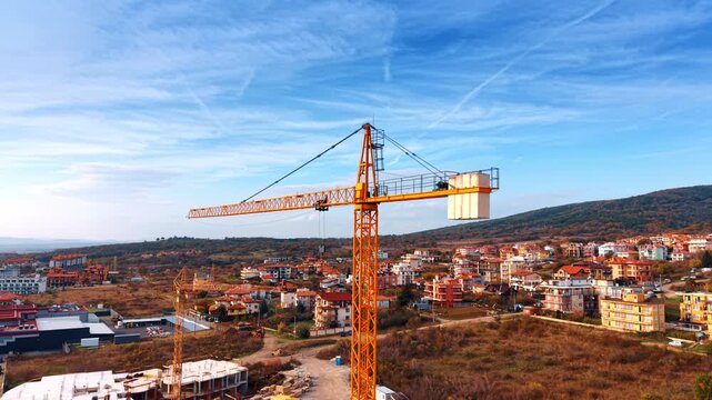 Tower crane on construction site with residential backdrop. Elevated view of a standing tower crane overlooking an undeveloped area and distant town.
