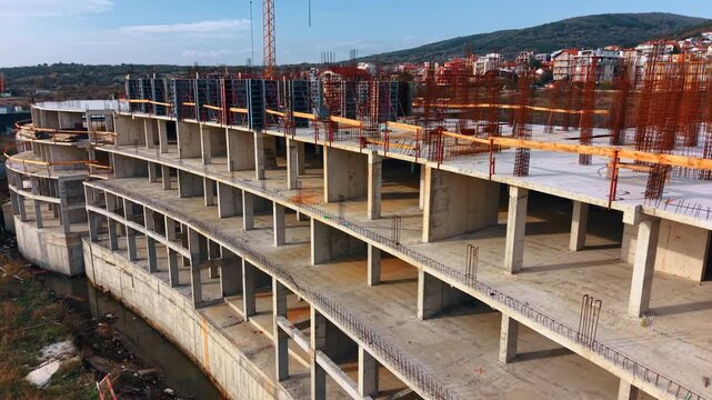 Concrete building frame under construction with steel rebar. Aerial view of a multi-story concrete building structure with exposed rebar and formwork on a construction site.