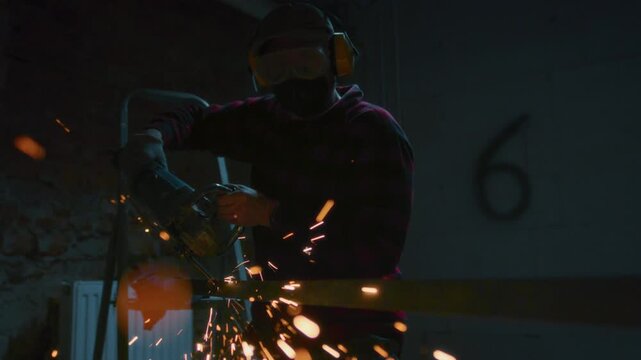 Male industrial or construction worker cuts metal with a angle grinder. Man uses circular saw at garage or workplace. Cutting raw material with flying red sparks at the factory or plant. Slow motion