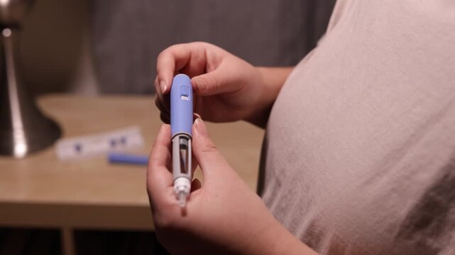 A horizontal close up shot. A young woman primes the pen injector, preperes it for injection
A young woman primes pre-filled pen injector with semaglutide