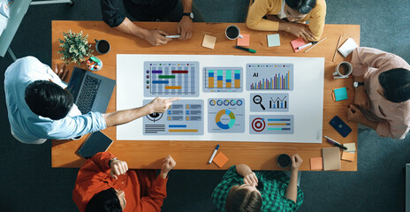A diverse group collaborates in a modern office, focusing on a digital dashboard and project...