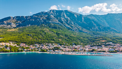 Stunning Croatian coastal town nestled beneath dramatic mountain range with turquoise Adriatic Sea, marina and Mediterranean architecture © Yuliko