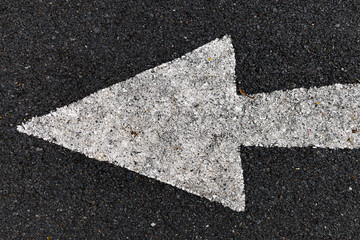 Fototapeta premium High angle view of a white painted arrow on dark asphalt road surface indicating travel direction.
