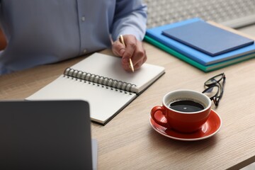 Man working at wooden table with cup of coffee in office, closeup