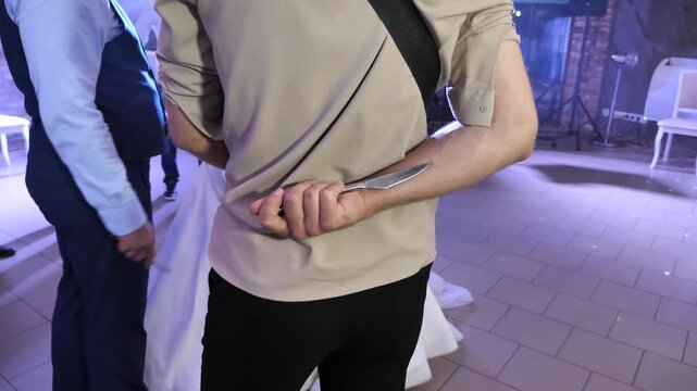 A young man hides a table knife behind his back during the reception.