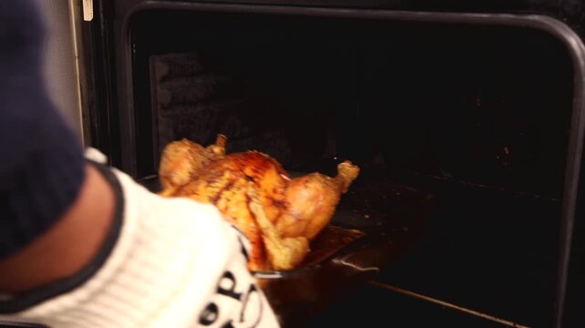 Une personne sortant un poulet r&ocirc;ti du four avec un gant.