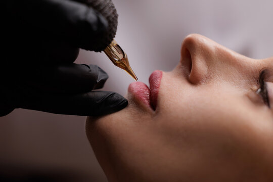 closeup of lip tattoo procedure on young female with tattoo machine, beauty cosmetic concept