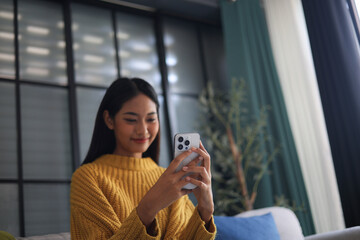 Fototapeta premium Relaxed woman sitting on the couch using phone at her home.
