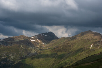 Fototapeta premium Dramatic mountain landscape with green slopes, rocky peaks and storm clouds overhead