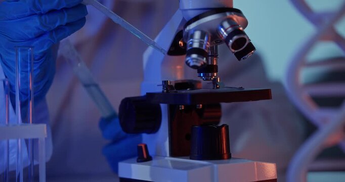 Scientist adjusts microscope focus and slide under cool blue lab lighting, gloved hands turning knob beside test tube rack and dna helix model in closeup motion sequence.