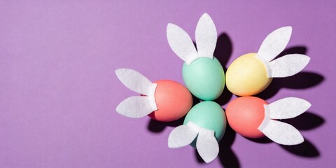 Fototapeta premium Flat lay pastel Easter eggs with felt bunny ears and bold shadows on purple background, modern spring holiday template with large copy space for poster or banner