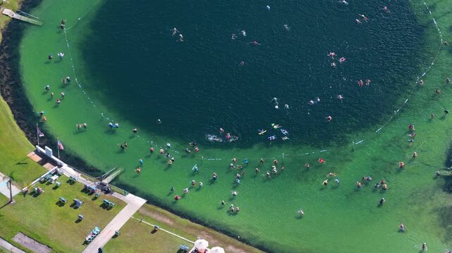 Aerial landscape of Warm Mineral Springs in North Port, Florida, featuring saturated blue water crowded with swimmers. Nature based wellness destination.