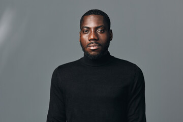Obraz premium African man portrait with serious expression wearing black turtleneck sweater in creative conceptual visual style on gray background. Studio shot with focused lighting and neutral tone.
