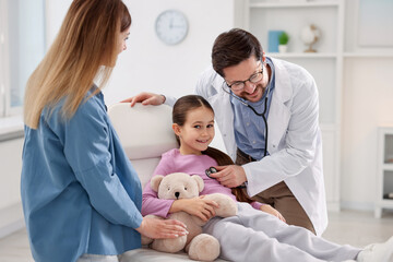 Obraz premium Little girl and her mother having appointment with pediatrician in hospital. Doctor checking child with stethoscope