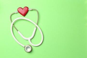Fototapeta premium Measuring blood pressure. Stethoscope and heart figure on light green background, top view. Space for text