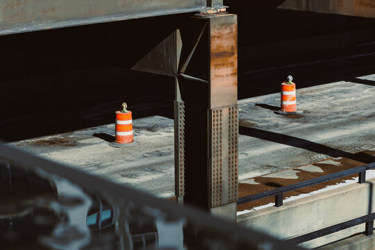 Construction site showing support beams and orange cones while workers carry out tasks during the afternoon near a busy highway