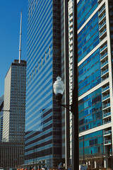 Obraz premium City buildings reflect sunlight on a clear day in downtown area with tall skyscrapers and streetlamps lining the road
