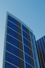 Obraz premium Building reaches towards the clear sky in a city with glass windows reflecting the sunlight and showcasing modern architecture during a bright day