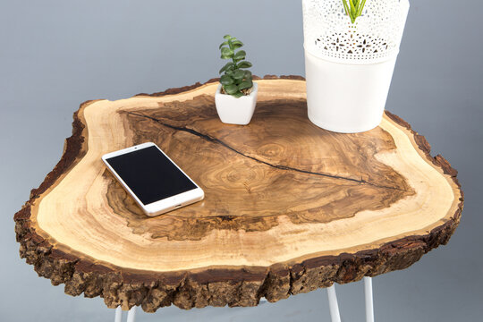 A wooden table displays a phone, plants, and a white pot. Live Edge of a walnut. slab wood