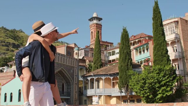 Joyful heterosexual couple share piggyback ride in colorful town, laughing and enjoying bright summer vacation moments. Concept: connection, happiness, freedom. Romantic couple have fun central asia