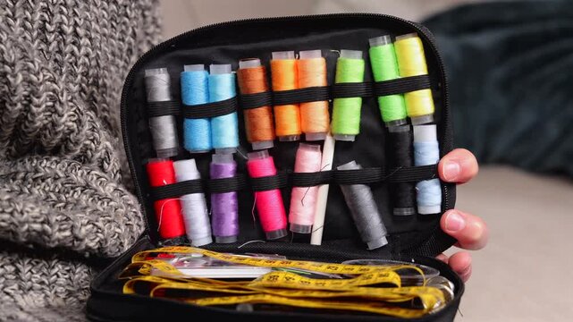 Une personne en train de choisir une bobine de fil color&eacute;es dans une trousse &agrave; couture traditionnelle.