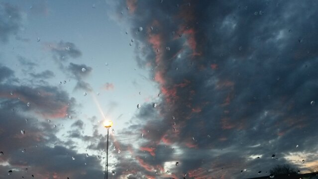 A beautiful sunset with rain and colorful clouds under the light of a streetlamp.
