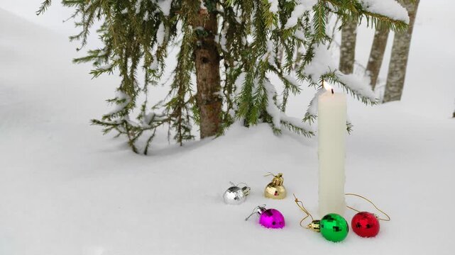A candle burns in the snow with Christmas decorations ( slow motion )