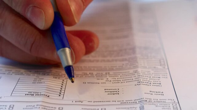 Hand Signing Paper Form Closeup.hand holding blue pen marking checkboxes on tax form document, concept of financial reporting, filing, audit and personal income declaration.