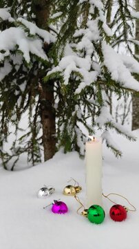 A candle burns in the snow with Christmas decorations