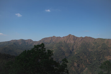 Obraz premium Mountain ridge landscape under clear blue sky, scenic highland terrain with forested slopes and rugged peaks in natural daylight.