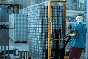 Worker operating a pallet jack to move stacked cans in a food production warehouse Focus on...