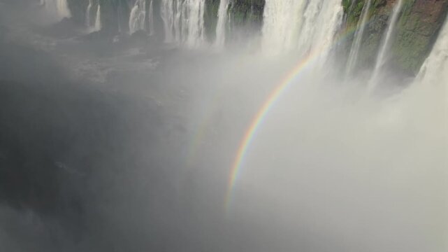 Panoramic view of multiple waterfalls through thick mist and water spray, with vivid double rainbow at Argentina-Brazil border