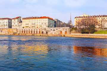 Obraz premium Murazzi del Po embankment along the Po River in Turin, Italy. Historic area features stone arches reflecting on the water beneath the iconic Mole Antonelliana tower