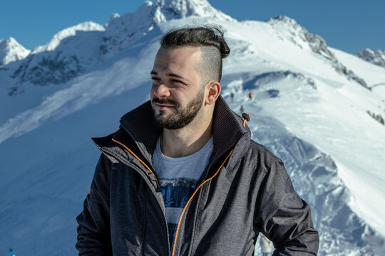 Portrait of a man wearing a warm jacket standing against a backdrop of snow-covered mountain peaks.