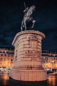Low angle shot of a majestic bronze statue on a pedestal, set against a dark night sky in a city plaza.