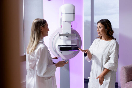 Female tech in lab coat showing purple backlit mammogram while female patient gesturing, copy space