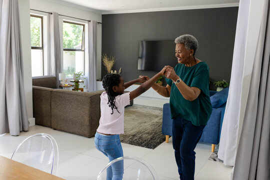 Senior woman wearing wristwatch, Youth girl dancing, holding hands in living room on rug near sofa