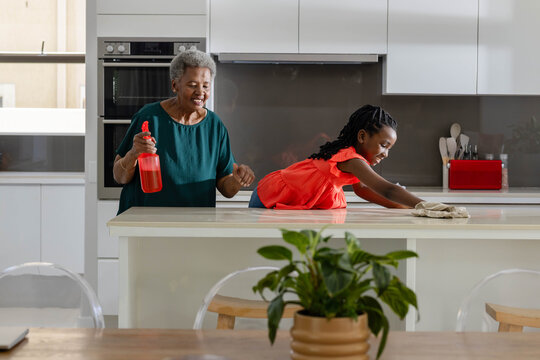 Senior, Youth African women in green top, red dress cleaning kitchen island with spray and cloth