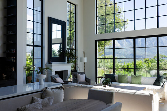 Light L-shaped sectional sofa is anchoring sunlit living room with coffee table, fireplace, plants