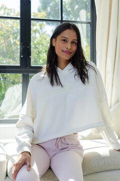 African American woman posing on sofa by black window, wearing hoodie and pink drawstring pants
