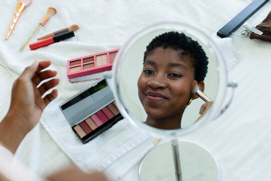 Round tabletop mirror is reflecting while makeup brushes and palettes are resting on towel at bed