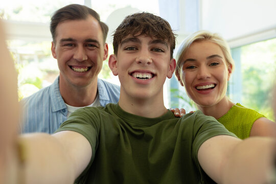 Family with teenage son taking selfie with smartphone in bright living room with large windows