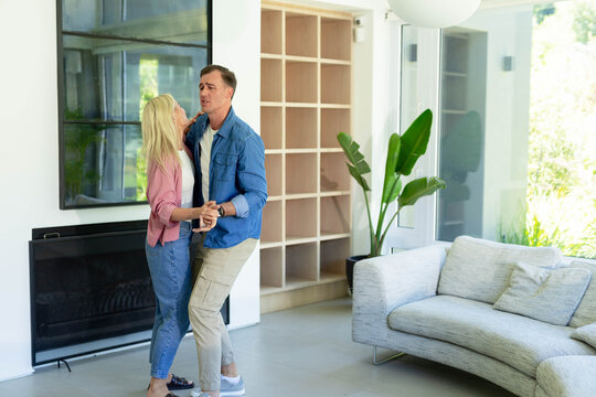 Couple dancing closely in bright living room near dark-framed mirror, low fireplace, plant