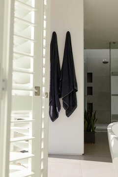 Two charcoal towels are hanging on hooks near glass shower while sunlight is casting shadows