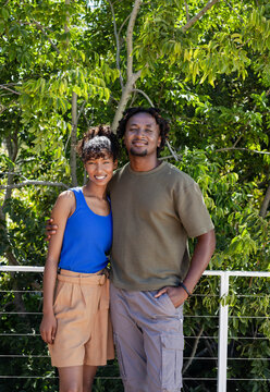 African American couple smiling on balcony, wearing tank top and cargo pants, holding cable railing