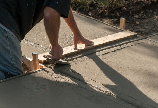 Canada, BC, Ladner.  Concrete worker leveling cement sidewalk.